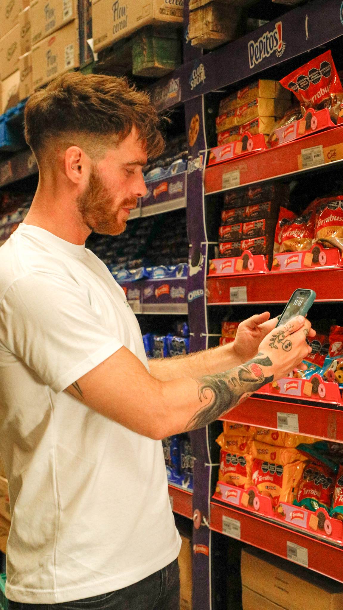 Znapper de remera blanca cargando datos en el celular frente a una góndola de galletitas.